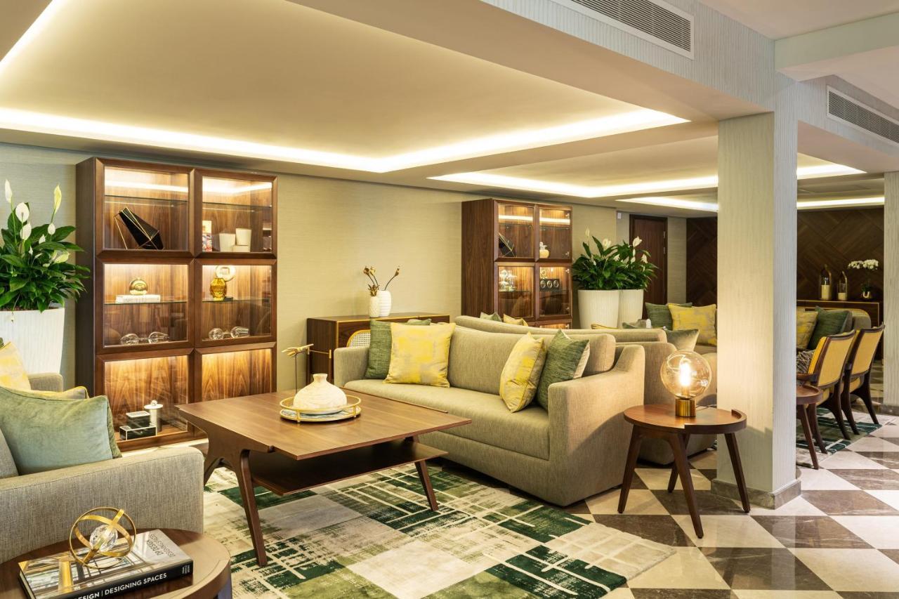 เลอ เมริเดียน ดูไบ โฮเต็ล แอนด์ คอนเฟอเรนซ์ เซ็นเตอร์ Hotel ภายนอก รูปภาพ The photo depicts a modern and elegantly designed lounge or living space. It features a light-colored sofa adorned with yellow and green cushions, and a coffee table in front of it. There are wooden shelves in the background, showcasing decorative it