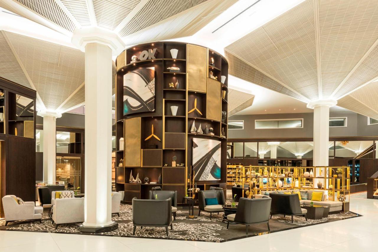 เลอ เมริเดียน ดูไบ โฮเต็ล แอนด์ คอนเฟอเรนซ์ เซ็นเตอร์ Hotel ภายนอก รูปภาพ The photo depicts a modern lounge or waiting area, characterized by a sleek and contemporary design. A prominent feature is a tall, circular shelving unit that displays various decorative items and art pieces, incorporating elements of gold and abstr