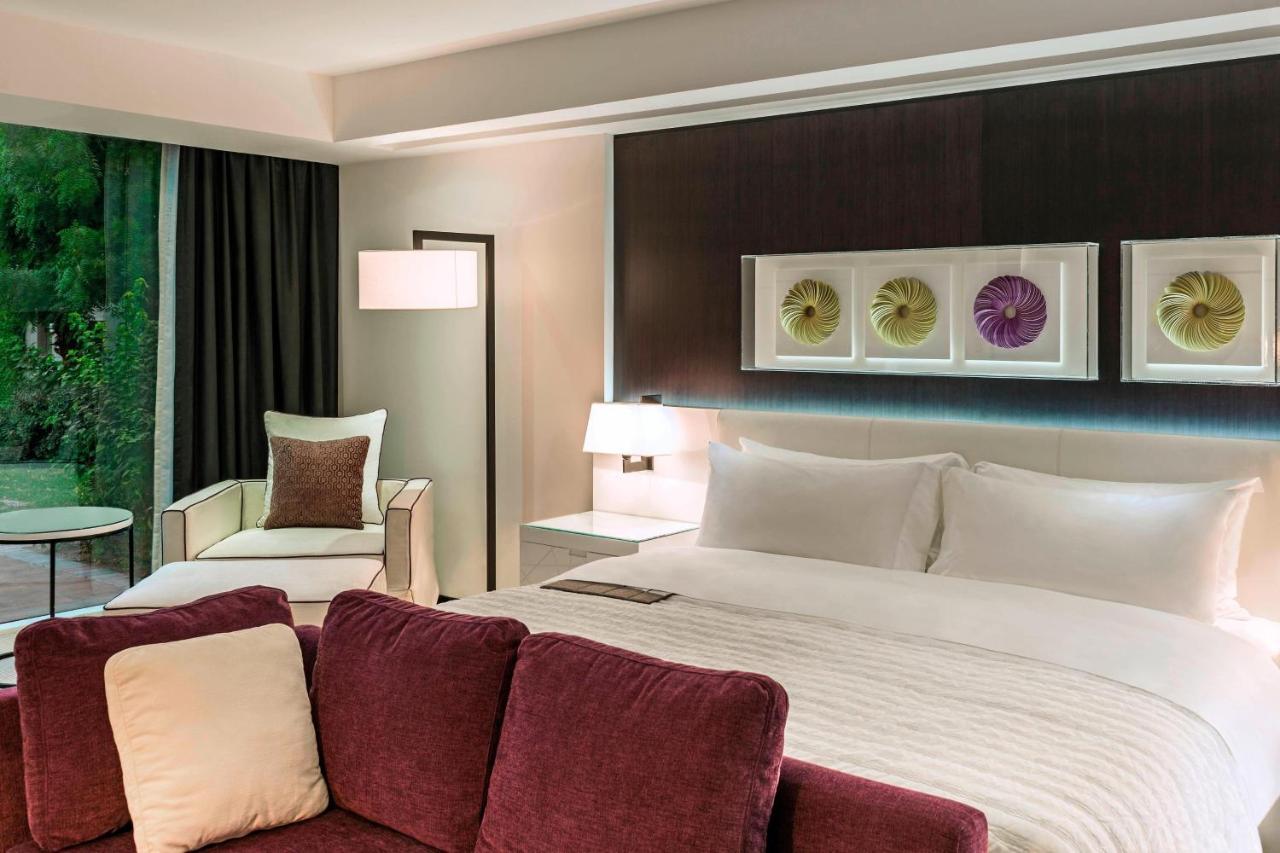 เลอ เมริเดียน ดูไบ โฮเต็ล แอนด์ คอนเฟอเรนซ์ เซ็นเตอร์ Hotel ภายนอก รูปภาพ The photo depicts a modern hotel room. It features a large bed with white bedding and elegant headboard. To one side, there's a comfortable armchair and a small round table. The room has dark curtains, allowing for a cozy atmosphere, and a decorative