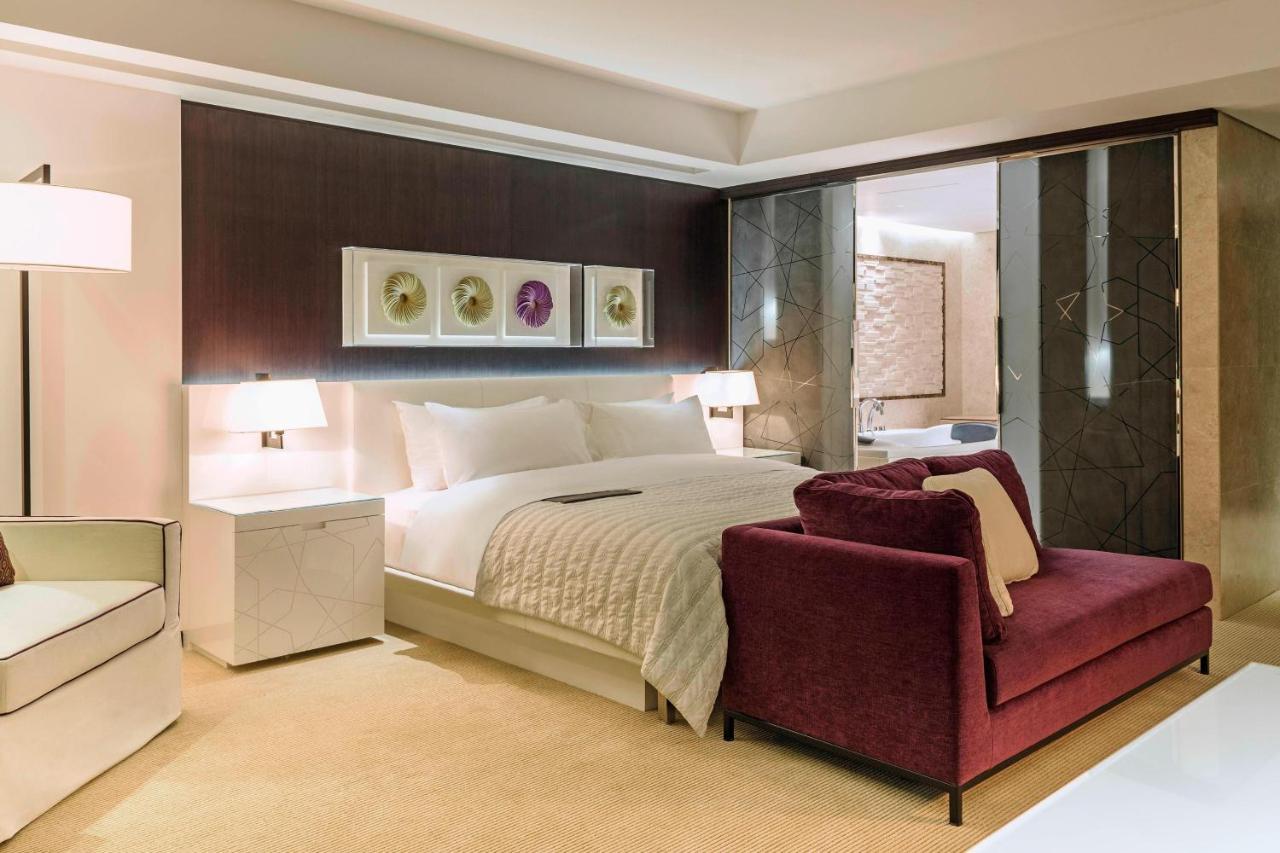 เลอ เมริเดียน ดูไบ โฮเต็ล แอนด์ คอนเฟอเรนซ์ เซ็นเตอร์ Hotel ภายนอก รูปภาพ The photo shows a modern hotel room featuring a spacious layout with a large bed, dressed in white linens, positioned against a dark accent wall. On either side of the bed are stylish bedside lamps. There is a burgundy armchair in front of the bed, p