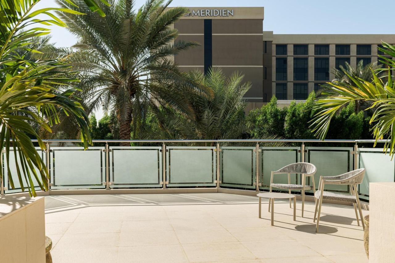 เลอ เมริเดียน ดูไบ โฮเต็ล แอนด์ คอนเฟอเรนซ์ เซ็นเตอร์ Hotel ภายนอก รูปภาพ The photo shows a balcony area with a paved floor and a railing. There are two white chairs positioned on the balcony. In the background, there is a building that appears to be part of a hotel, identifiable by the name "Le Meridien" on its exterior. 