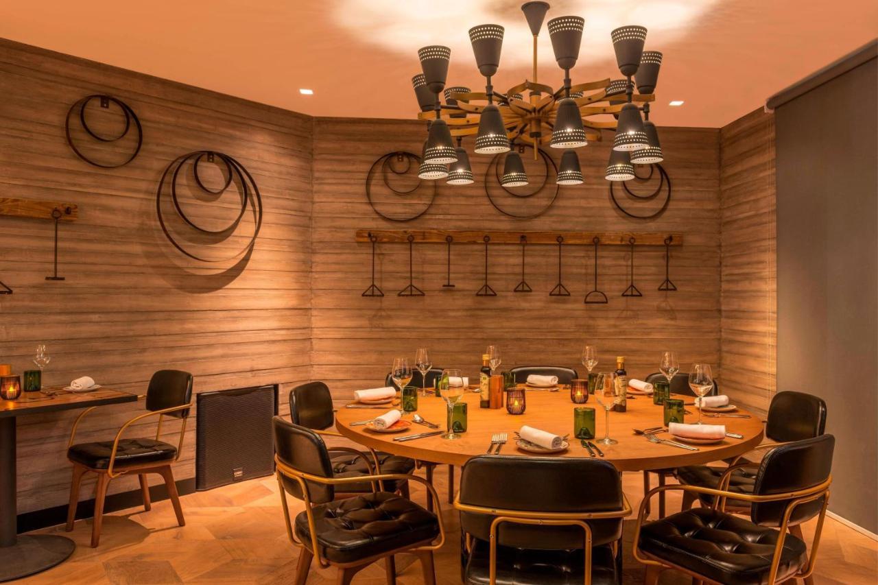 เลอ เมริเดียน ดูไบ โฮเต็ล แอนด์ คอนเฟอเรนซ์ เซ็นเตอร์ Hotel ภายนอก รูปภาพ The photo shows a modern dining room with a circular wooden table surrounded by stylish black chairs. The walls are adorned with a textured design and feature some circular decorations, possibly made of metal or wood. Above the table, there is a uniq